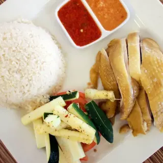 Plate of steamed chicken rice with vegetables and two dipping sauces